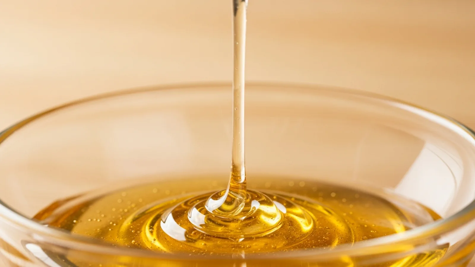 A thin thread of golden honey drawn up from a glass dish